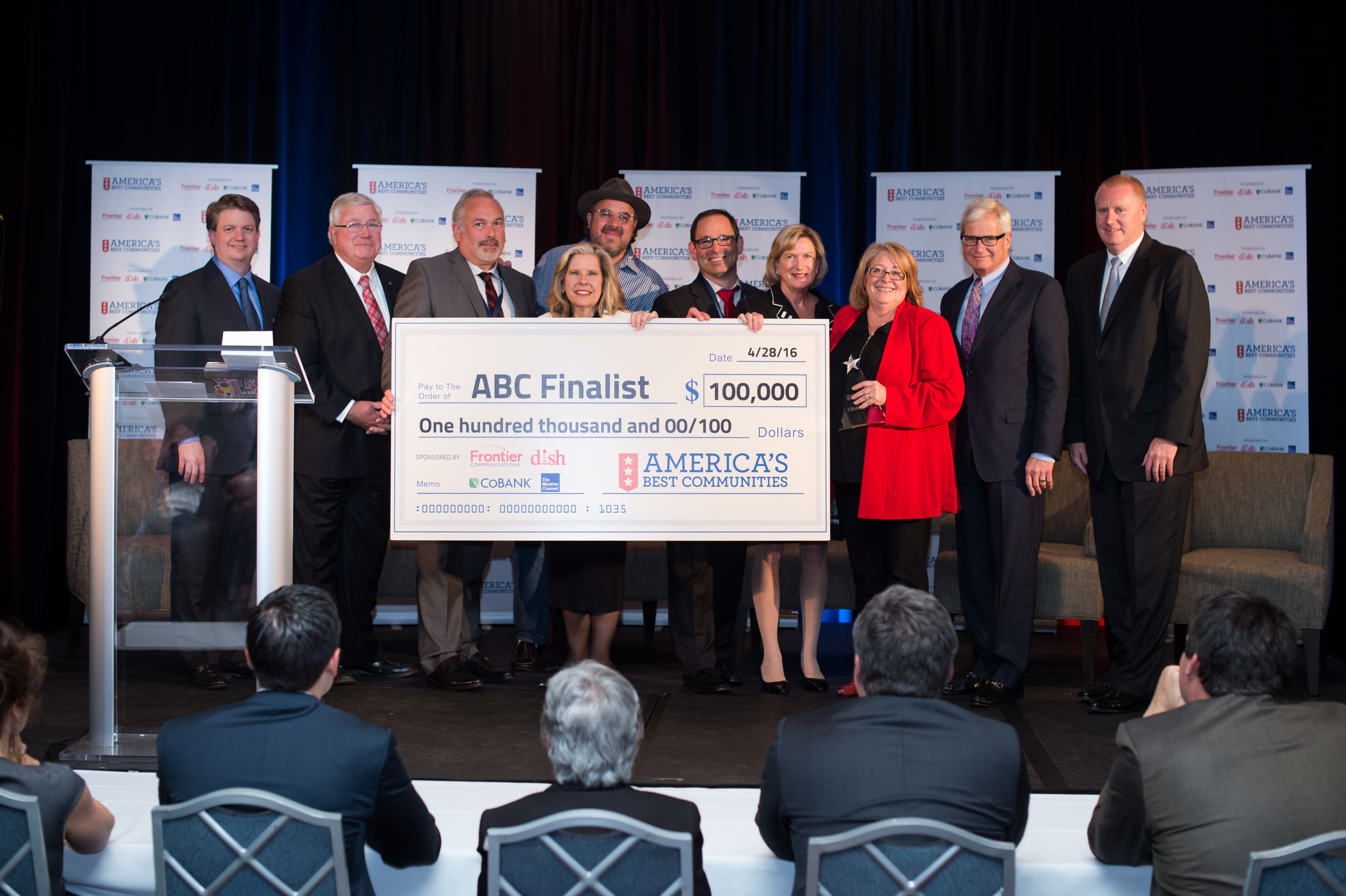 Group of people standing on stage holding an $100,000 check for the America's Best Communities competition