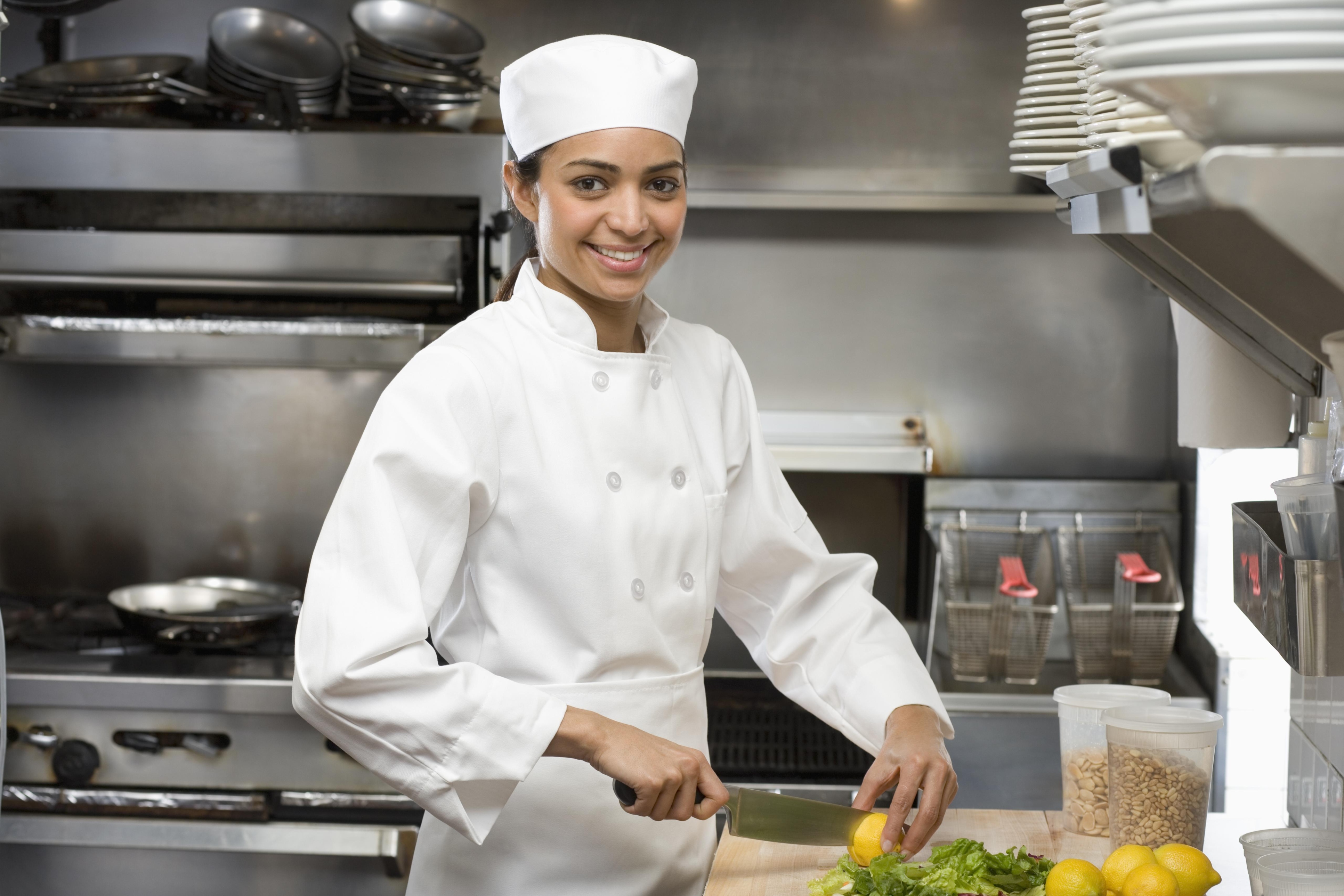 Waist-length view of a female chef working in a restaurant kitchen and smiling at the camera
